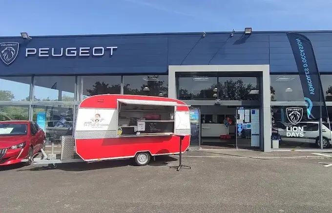 La caravane crêpes rouge et blanche garée devant une concession automobile
