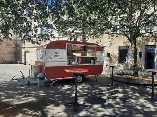 La caravane rouge et blanche à l'ombre d'un arbre, mange-debout installés devant